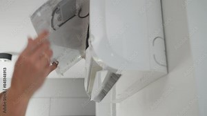 Maintenance of air conditioner unit. Technician checks air conditioning system mounted on white wall. Climate system with opened front cover revealing internal components. Repairing HVAC in apartment
