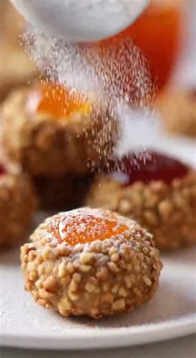🍪 Walnut Thumbprint Cookies with Jam Ingredients: ½ cup (1 stick) butter, softened ⅔ cup sugar 2 eggs (separated: yolks for dough, whites for coating) 1 teaspoon vanilla extract 2½ cups all-purpose flour 2 teaspoons baking powder 1 cup chopped walnuts (for rolling) Jelly or apricot preserves (for filling) Powdered sugar (for dusting) Instructions: Cream butter and sugar together in a bowl using a hand or stand mixer until light and fluffy. Add flour and baking powder gradually, mixing until com