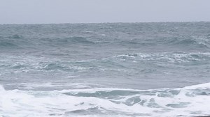 Two surfers in wetsuits try to catch a wave in a severe storm in the Pacific ocean in winter