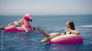 Happy woman chill in infinity pool with inflatable donut rubber ring, young married couple swim pink flamingo, have fun on background. Memories of together summer vacation trip, pool party