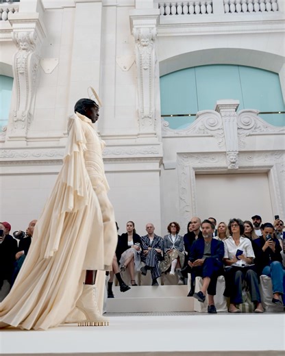 … eyes on the prize … akuol deng atem wears a tailored dress with corset detail, all hand pleated and stitched in an overlay of mixed muslins with a back panel embroidered with frayed strips of mixed horsehair canvas, muslin tulle bobbinet and organza. paired with the dress are heritage trainer heelless ankle boots with running spikes in muslin. thom browne couture 2024 collection. #thombrowne #thombrownecouture | THOM BROWNE.