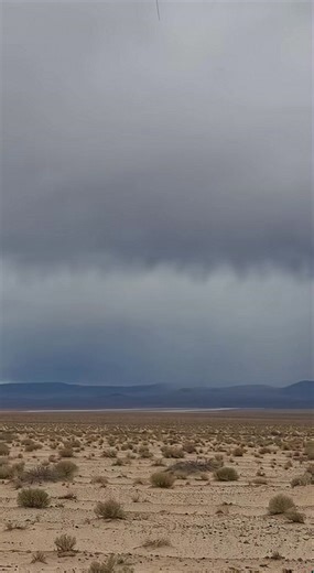 Vintage 16mm Archival Footage Of A Nuclear Explosion In The Desolate Desert ------------ ----------- ------------- This cinematic footage captures a chilling moment in a desolate, flat desert landscape under a heavy blanket of grey clouds. The scene begins with a sudden white streak descending from the heavens, triggering a blinding flash that illuminates the distant horizon. From the impact site, a massive mushroom cloud quickly ascends, characterized by a thick tan dust column that supports a 