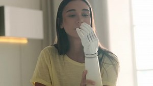 Close up woman looking to her high-tech bionic arm, caucasian girl examines and checking movement of fingers, admires artificial prosthetic limb hand at home