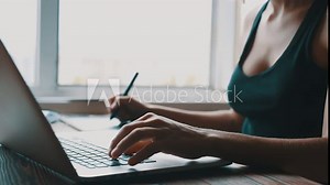 A young girl designer works on the computer and draws on a graphics tablet at the window