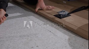 Close up view of a person using a rubber mallet and floor clamp to align and secure wooden floorboards, highlighting craftsmanship and precision. Stock Video