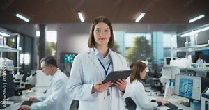 Portrait of an Attractive Female Scientist Posing for Camera, Smiling. Young Biologist Standing in a White Coat, Using a Tablet Computer in a Modern Laboratory, Researching Pharmaceutical Products
