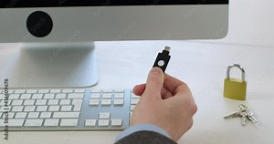 Close-up, a man holds an electronic access key with his fingers on the background of a computer keyboard and a lock with keys. Modern data access encryption systems.