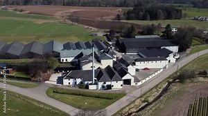 Aerial view of Fettercairn whisky distillery on a sunny spring day, Aberdeenshire, Scotland. Rotating right to left around the distillery with zoom out.
