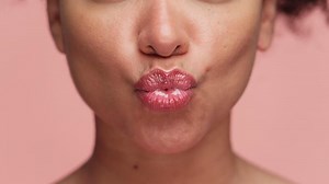 Close-up of woman puckering lips for kiss on pink
