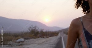Beautiful authentic young woman in 20s walking down highway in desert - walks out of frame - rack focus