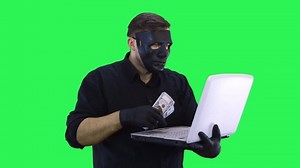 A masked computer hacker is talking via video link and showing the money earned.
