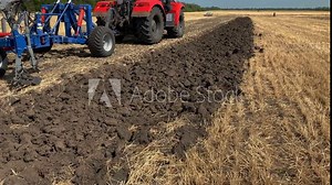 Rear view a large tractor with a plow standing in a field. Start tillage after harvest. Work of agricultural equipment and farmers.