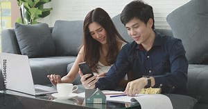 Lovely Asian couple using a notebook computer and smartphone to managing their startup business.
