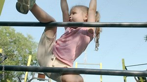 Little girl climbs gymnastic ladder on open sports ground on outside. Cute little girl crawls on vertical sports ladder in city park on sun day. slow motion