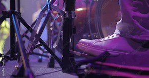 Close-up of the legs of a drummer in sneakers on stage. The drummer kicks the bass drum pedal. Musical group at backgound, live concert. Slow motion