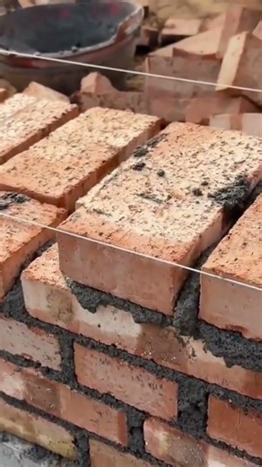 applying a thick layer of grey cement mortar onto red clay bricks using a metal trowel tool today