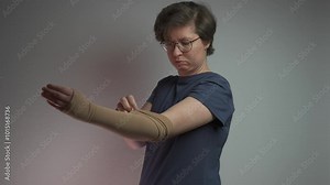 Prophylactics of thrombosis. Woman removes compression sleeve from left hand on gray background. Effective anti-thrombosis therapy involves compression sleeves to improve vein health and blood flow.