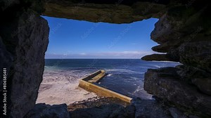 Time lapse of concrete block pier viewed from above through a medieval stone castle window on sunny cloudy day located in Easkey county Sligo along the Wild Atlantic Way in Ireland.
