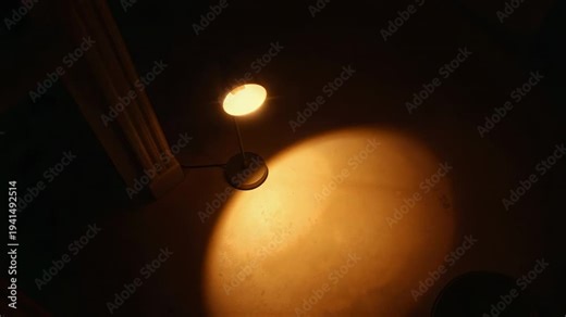 Desk lamp tilting shade and camera panning, shifting warm circular floor light for lighting study