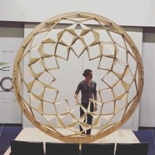 Kinetic installation: Chiris [“chai-ris”] is a transforming sculpture designed and built by three architects Jeffrey Montes, veanad and pucarl. The aim was to imagine how the technology and experience of an aperture mechanism could be scaled up and translated into architecture. An innovative, folding origami skin adds a rich third dimension and a shifting pattern of light and shadow. Chiris is comprised of over 100 wooden arms; each CNC milled, hand-routed, sanded smooth and completed with plast