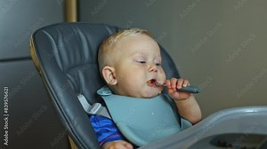 A little boy is sitting in a high chair, eating porridge, and his mother is trying to feed him with a spoon. Baby food. The first meal for a child.