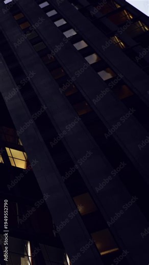 People can see a tall building at night with some lights on in windows. The view is from below and shows the buildings structure against the dark sky.