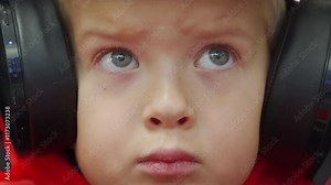 Child wearing red dragon costume in bluetooth wireless large over ear headphones. Little boy in animal kigurumi pajamas playing on video game console at home. Concentrated face of child.