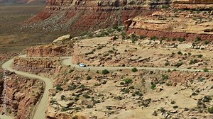 Car Driving On Dirt Road Carved Out Of Steep Rock Cliffs. Moki Dugway On State Route 261 In San Juan County, Utah. wide aerial