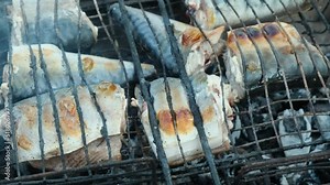 Close-up fish is grilled on charcoal outdoors. Pieces of mackerel is fried on old metal grill over open fire. Camping food concept.