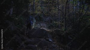 Young man hiking up a steep rocky trail in the dark with a flashlight. Hiker walks up a rocky hill in the night with a flashlight.