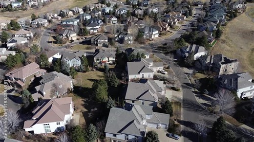 Detached homes near Saddle Rock Golf Club follow winding streets and cul-de-sacs with visible garages, parked vehicles. Roof textures and tree shadows blend into open fairways, Aurora, Colorado