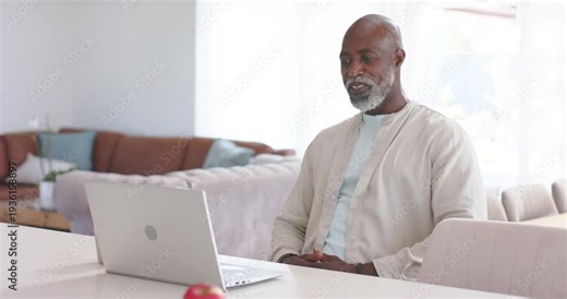African male senior getting call waving and greeting contact at home with silver laptop, copy space