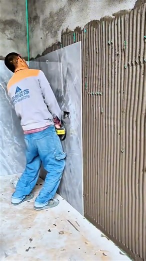 Worker installing large wall tiles using adhesive comb