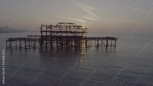 West Pier Brighton early morning close up eye level, slow pan left to right of remaining rusting structure. Sunrise shining through structure reflecting and creating shadows on calm sea East Sussex UK