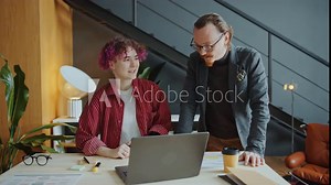 Male CEO explaining business plan on laptop screen to young female employee with prosthetic arm when working together at desk in modern office
