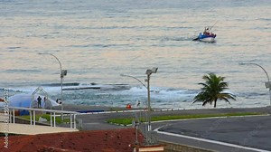 Peaceful Guanabara Bay ocean waves splashing shore near historic Fort Copacabana tourist attraction and fishing boat vessel driving behind palm trees in tropical Rio de Janeiro, Brazil coast