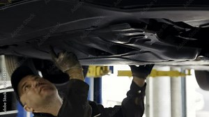 Car mechanic dismantles plastic car engine guard and removing old plastic sump guard under the vehicle at the service station