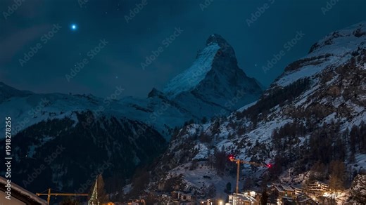 Timelapse over Zermatt in Switzerland at night. Swiss ski resort. The Matterhorn in the background during starry night with Orion constellation visible over the Matterhorn. Famous alpine village.