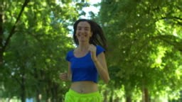 Happy female runner jogging during outdoor workout in summer park....