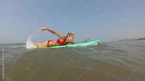 A young woman learns to surf and falls off a surfboard. Girl surfer in the sea
