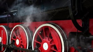 Side view of a steam locomotive wheels at a railway station. Puffs of steam against the background of a train. Working train museum.