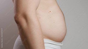 A man with a bare torso in white underpants inflates and sticks out his big belly. The concept of weight gain, overeating and obesity. Side view