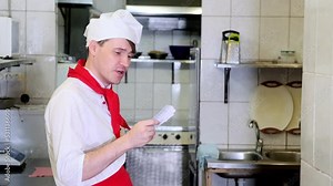 Chef taking order slip in commercial kitchen. Caucasian chef reads out an order for his subordinates in restaurant kitchen
