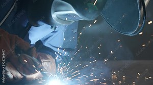 Close-up blacksmith welder in protective mask works with metal using a welding machine, bright sparks and flashes in slow motion