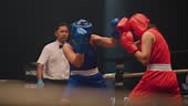 An Asian boxing referee looking over the fight between two female...