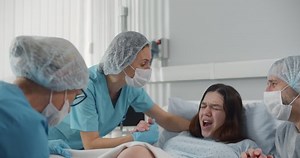 Doctor and nurses helping young pregnant woman in labor. Pregnant female in delivery room pushing during contractions giving birth with medical team assistance