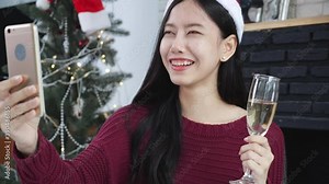 Young asian woman selfie video call online with friends and show glass in Christmas day on phone at home with social distancing, new normal, female video conference, communication and holiday concept.