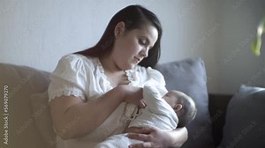 Madre sentada amamantando a bebé desde su pecho en posición de cuna viendo a su hijo tomando leche materna