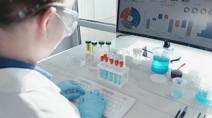 A dedicated scientist in a laboratory setting works meticulously with test tubes and monitors data analysis on a computer screen, reflecting advanced scientific research in medicine.