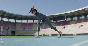 Female sports runner girl stretching and warming up on synthetic track. Out of focus open field generic stadium in the backgorund.